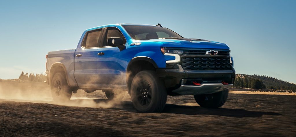 2026 Chevrolet Silverado driving across a dusty off-road landscape, highlighting its rugged build and comfortable, driver-focused interior
