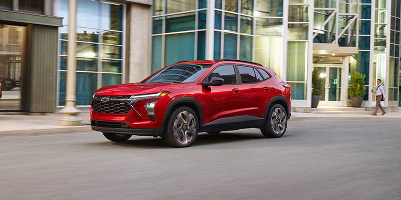 A 2026 Chevrolet Trax drives down a city street, showcasing its sleek design and urban environment.