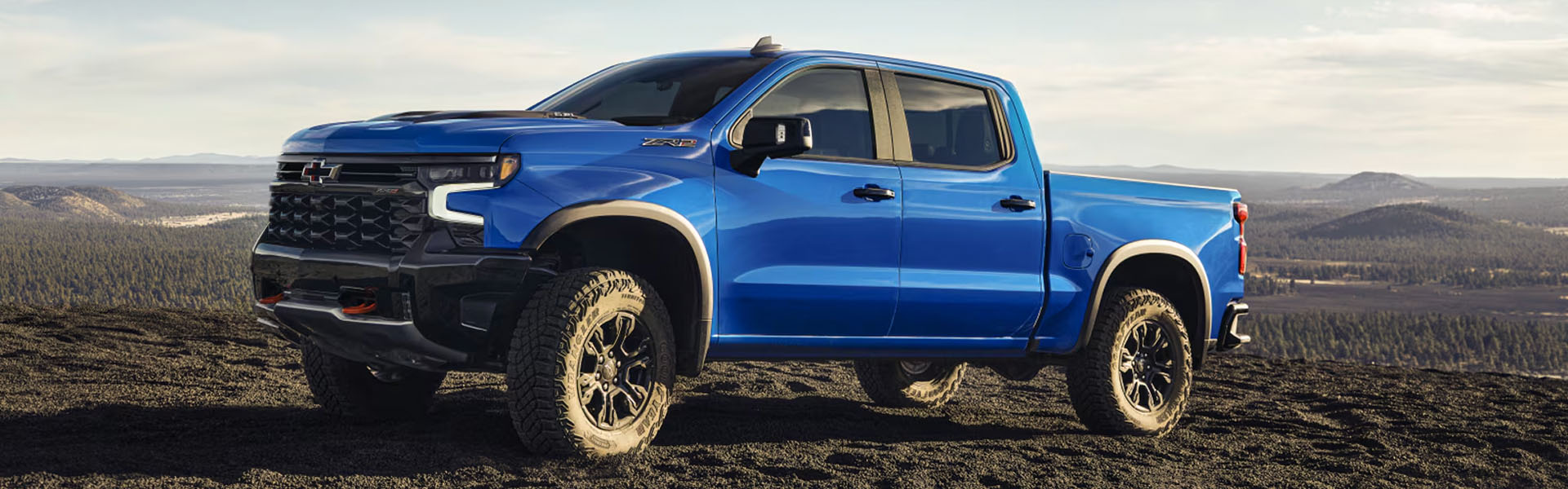2026 Chevrolet Silverado 1500 in blue parked on rocky terrain with mountains in the background.